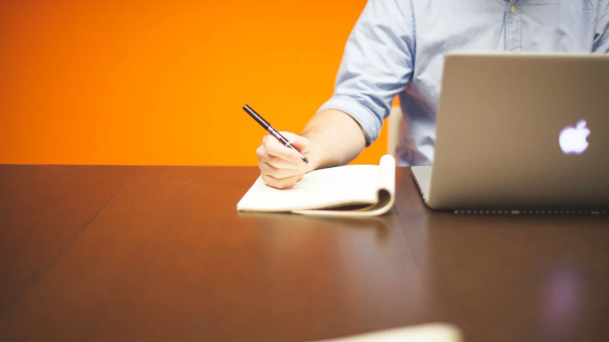 Notitieboek en pen naast een geopende laptop op een bureau